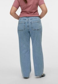 Jeans de tiro alto, azul claro, con corte recto, dos bolsillos traseros y detalles de costura visibles. Combinados con una blusa rosa.