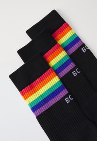 Calcetines negros con rayas horizontales en los colores del arcoíris: rojo, naranja, amarillo, verde, azul y púrpura en la parte superior; textura acanalada; marca blanca.