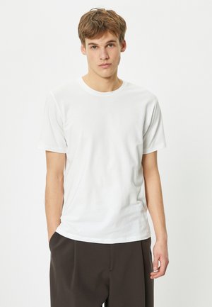 Witte katoenen t-shirt met korte mouwen, ronde halslijn, getailleerde pasvorm, gladde textuur, gecombineerd met losse, donkere broeken.