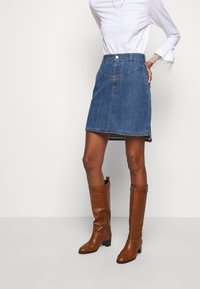 Blå denim A-linje kjol med fickor, knäppning med knapp och längd ovanför knäna; matchad med bruna läderstövlar till knäna.