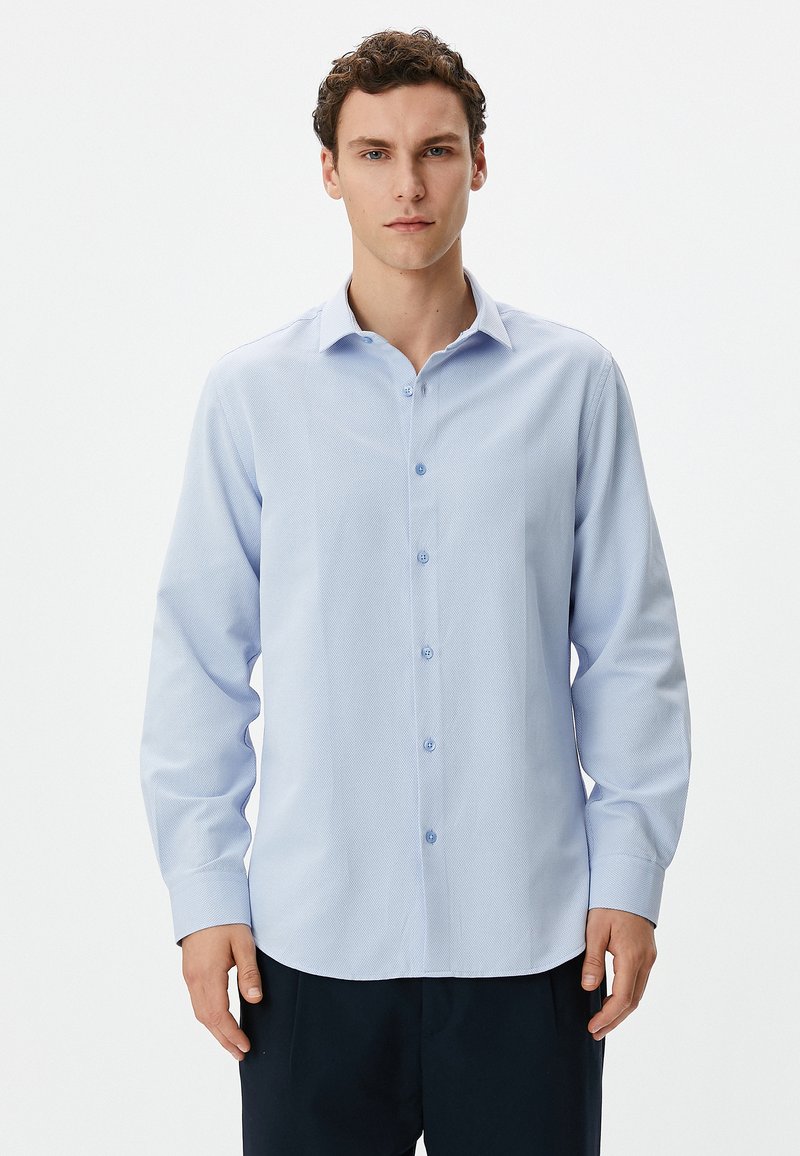 Camisa de botón de manga larga en azul claro con un patrón texturizado, que presenta un cuello clásico y botones en azul claro. Corte ajustado.