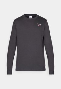 Tmavě šedá mikina vyrobená z měkké tkaniny, s žebrovaným kulatým výstřihem a manžetami. Malé logo Reebok na horní levé části hrudníku.