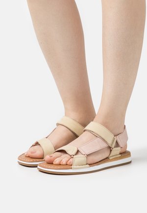 Tan and light pink flat sandals with Velcro straps; open toe design, cushioned footbed, and white rubber sole with brown accents.