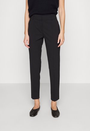Pantalons ajustés noirs avec une coupe droite, mettant en valeur des détails fendus sur les côtés et une texture lisse. Associés à des chaussures plates noires.