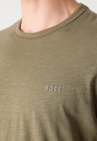 Olívazöld póló puha anyagból, kerek nyakkivágással és egy kis, texturált "BOSS" logóval a mellkasi bal oldalon.