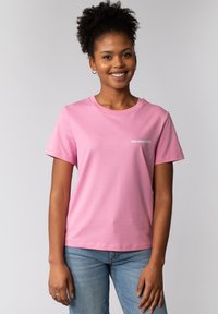 Roze katoenen T-shirt met een ronde hals en korte mouwen; heeft een witte grafische opdruk "SAG NIEMALS NIE" op de linkerkant van de borst.