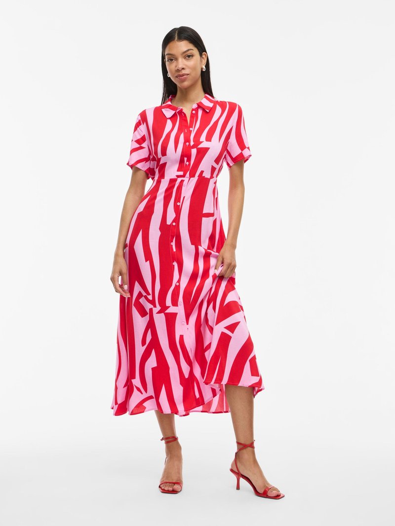 Punase ja roosa kirjadega kleit lühikeste käistega, nööbid ees ja voolav, keskpikk seelik. Ümber on punased rihmadega kontsad.