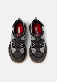 Scarpe da esterno grigie e nere con materiali testurizzati, lacci riflettenti e una suola robusta, con una soletta rossa e marchio sul tallone.