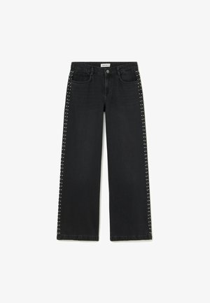 Jeans anchos negros con tachuelas plateadas que corren verticalmente a lo largo de las costuras exteriores y en los bolsillos delanteros, con cierre de botón y cremallera.