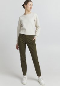 Light beige sweatshirt with a crew neckline and ribbed cuffs, paired with dark green tailored pants featuring dual buttons and side pockets.