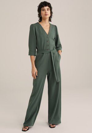 Tuta verde a maniche lunghe con scollo a V, bottoni frontali e cintura annodata in vita. Presenta pantaloni a gamba larga. Texture liscia, design minimalista.