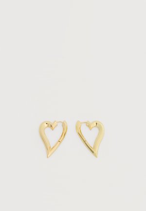 Paire de boucles d'oreilles en forme de cœur ouvert en ton or sur fond blanc uni.
