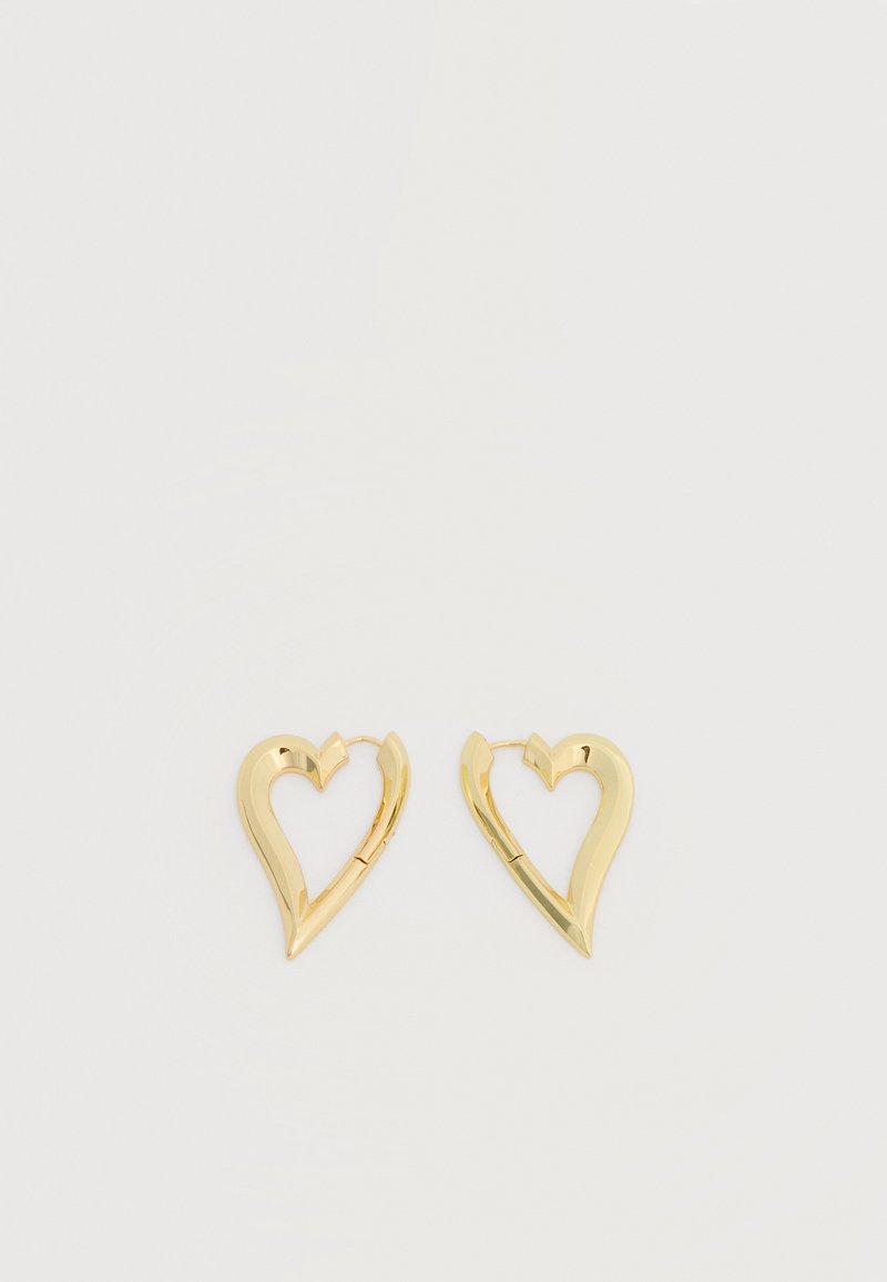 Ζεύγος χρυσών σκουλαρικιών σε σχήμα ανοιχτής καρδιάς, σε απλό λευκό φόντο.