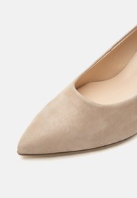 Chaussure plate en daim beige à bout pointu avec doublure intérieure lisse, photographiée sur un fond clair, montrant les détails de face et de côté.
