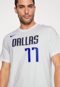 Hvid kortærmet t-shirt med "DALLAS" i gråt og "77" i blåt med prikmønstre på fronten. Nike-logo i blåt på skulderen.