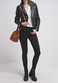 Black leather jacket over a white top, paired with black skinny jeans, black ankle boots, and a brown bucket bag.