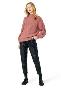 Maglione oversize rosa a trecce con polsini a costine abbinato a pantaloni neri in pelle a gamba affusolata e stivaletti neri.