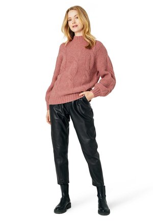 Överdimensionerad rosa kabelstickad tröja med ribbade ärmslut, tillsammans med svarta läderbyxor med tapered passform och svarta ankelstövlar.