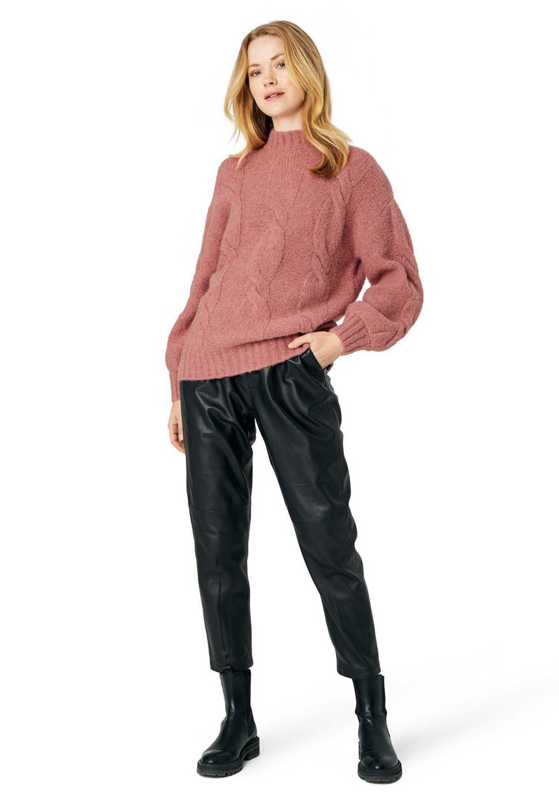 Maglione oversize rosa a trecce con polsini a costine abbinato a pantaloni neri in pelle a gamba affusolata e stivaletti neri.