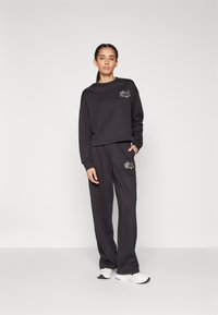 Felpa corta grigio scuro con logo e pantaloni larghi abbinati. Entrambi i capi sono realizzati in tessuto morbido, che si abbinano a scarpe da ginnastica.