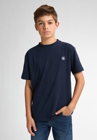 Marineblauwe katoenen T-shirt met korte mouwen, ronde halslijn en een klein logo-opdruk op de borst. Gecombineerd met blauwe denim jeans.