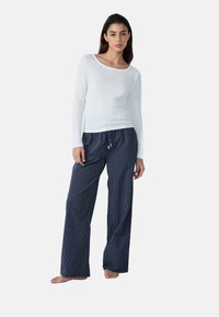 Top bianco a maniche lunghe con una texture a coste e un ampio scollo, abbinato a pantaloni larghi blu navy con strisce verticali bianche e un cordino.
