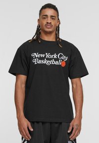 Sort bomulds T-shirt med hvid tekst, der står "New York City Basketball" og et orange basketballgrafik. Loose fit, korte ærmer.