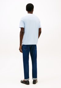 Šviesiai mėlynas trumpomis rankovėmis marškinėlis su standartiniu prigludimu, derinamas su tamsiai mėlynomis džinsais. Džinsai turi atlenktą kraštą ir dvi kišenes gale. Juodi batai.