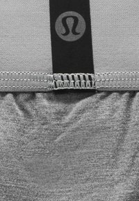 Tela atlética gris con un aspecto texturizado, que presenta una banda elástica negra con un logo en la parte superior y detalles cosidos en la costura.