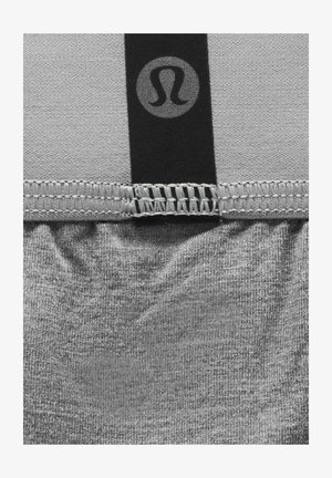 Tessuto atletico grigio con un aspetto texturizzato, caratterizzato da un elastico nero con un logo nella parte superiore e dettagli cuciti sulla cucitura.