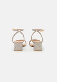 Sandalias de tacón con un tacón cuadrado, cubiertas de brillantes multicolores, con correas de tobillo entrecruzadas y una plantilla beige.