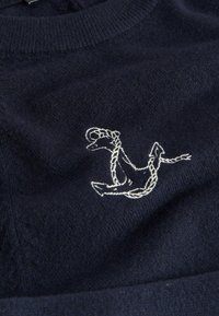 Pull en mailles de couleur marine avec un motif d'ancre brodé blanc, présentant un col rond et un tissu texturé.