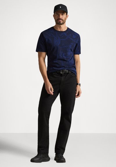 T-shirt azul-marinho com estampa gráfica, calças pretas e sapatos pretos. Apresenta gola redonda e mangas curtas. Design simples com corte casual.