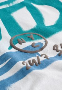Weißer Stoff mit türkisfarbenen und blauen abstrakten Designs. Mit einem kreisförmigen "NYC"-Logo in Braun. Der Text umfasst "24/7" in Braun.