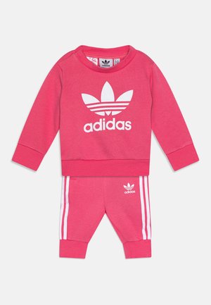 Tuta in cotone rosa composto da una felpa con colletto a girocollo con logo Adidas bianco e pantaloni coordinati con strisce bianche e logo sul lato.
