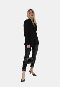 Blazer nero, forma aderente, con un solo bottone. Jeans scuri con orli decorati e una piccola borsa nera con motivo coccodrillo. Sandali neri con tacco alto.