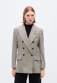 Διπλόπετο σακάκι με μοτίβο ψαλιδωτής κανάτας σε μπεζ και μαύρο χρώμα, με φαρδιές πέτα, μαύρα κουμπιά και δύο μπροστινές τσέπες.