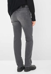 Persona che indossa jeans dritti grigi, un maglione nero e stivali neri con suola spessa, in piedi su uno sfondo bianco.