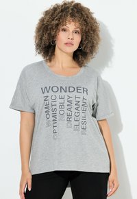 Šedé bavlněné tričko s vertikálním textovým designem v tmavě šedých písmenech obsahujícím "WONDER," "OPTIMISTIC," a "RESILIENT." Krátké rukávy, uvolněný střih.