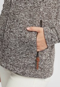 Brun och vit mönstrad tröja, med en dragkedjeficka med läderdrag. Mjuk textur, figurnära design och ribbade muddar.