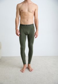 Green fitted leggings made of stretch fabric, featuring a black elastic waistband with "BJÖRN BORG" logo. Smooth texture, tapered design.