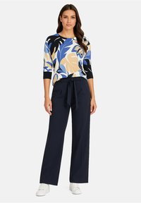 Pull multicolore avec des motifs floraux en bleu, noir et beige, associé à un pantalon large navy et des sneakers blanches.