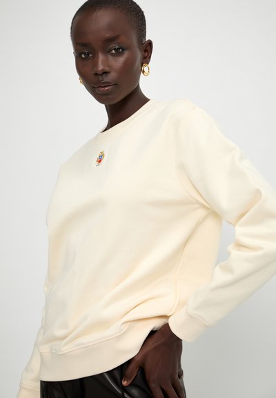Cremefarvet sweatshirt lavet af blødt stof, med rund halsudskæring og ribbede manchetter. Inkluderer et lille, farverigt broderet mærke på forsiden.