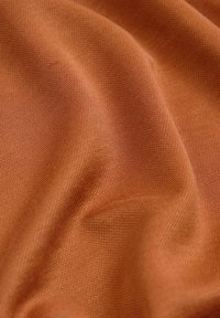 Tuva skatījums uz mīkstu, nedaudz krunkainu, oranžīgi brūnu austu audumu ar redzamu mazu teksturētu adījumu patterns.