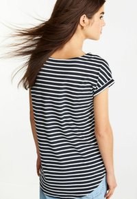 Marinblå och vit randig T-shirt med korta upprullade ärmar, mjukt tyg och en något rundad nederkant. Modell vänd bort, med flödande hår.