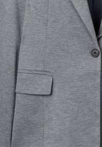 Blazer grigio in tessuto strutturato con colletto a revers, chiusura con un bottone e dettaglio del polsino piegato.