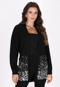 Schwarzer Cardigan mit langen Ärmeln, offenem Vorderteil und großen, mit Pailletten verzierten Taschen auf der Vorderseite, aus weichem Strickmaterial gefertigt.