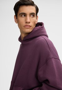 Lila Kapuzenpullover aus Baumwollstoff, mit einer großen Fronttasche, einer Kordelzugkapuze und einem lässigen Schnitt durch die überschnittenen Schultern.