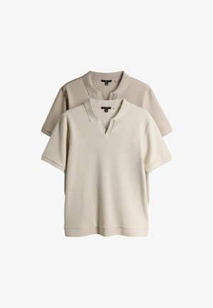 Dve pletené polo tričká s krátkym rukávom, jedno béžové vpredu a jedno svetlohnedé vzadu, zobrazené na bielom pozadí.