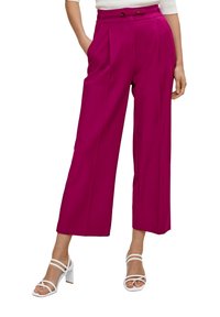 Fuksjowe spodnie o szerokich nogawkach z plisami, wysoki stan oraz podwójne zapięcie na guziki. Połączone z białymi sandałami na obcasie. Gładka faktura materiału.